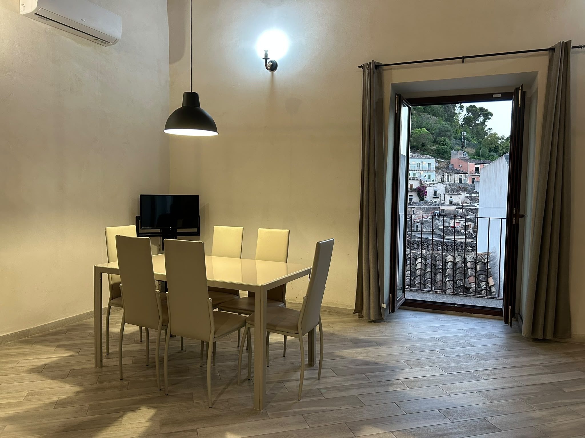 Tavolo da pranzo con porta finestra aperta sul balcone e vista sui tetti di Modica