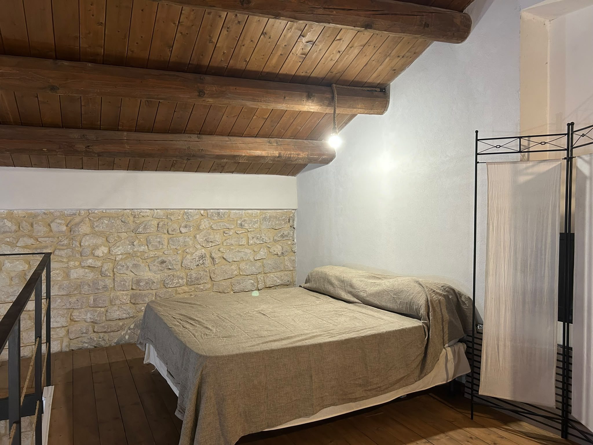 Soppalco con letto matrimoniale a baldacchino e parete in pietra a vista