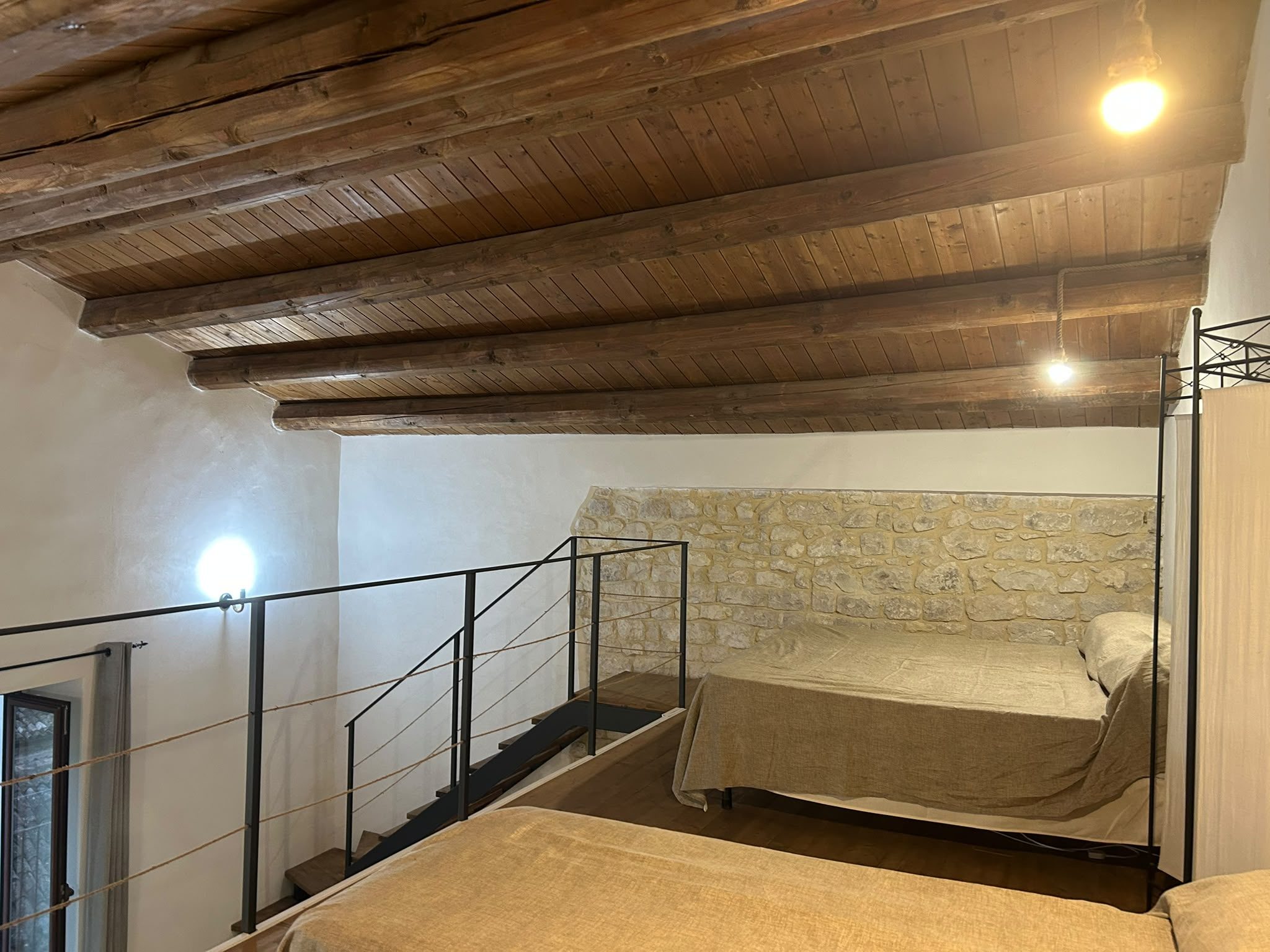 Soppalco con letto singolo, travi in legno e parete in pietra